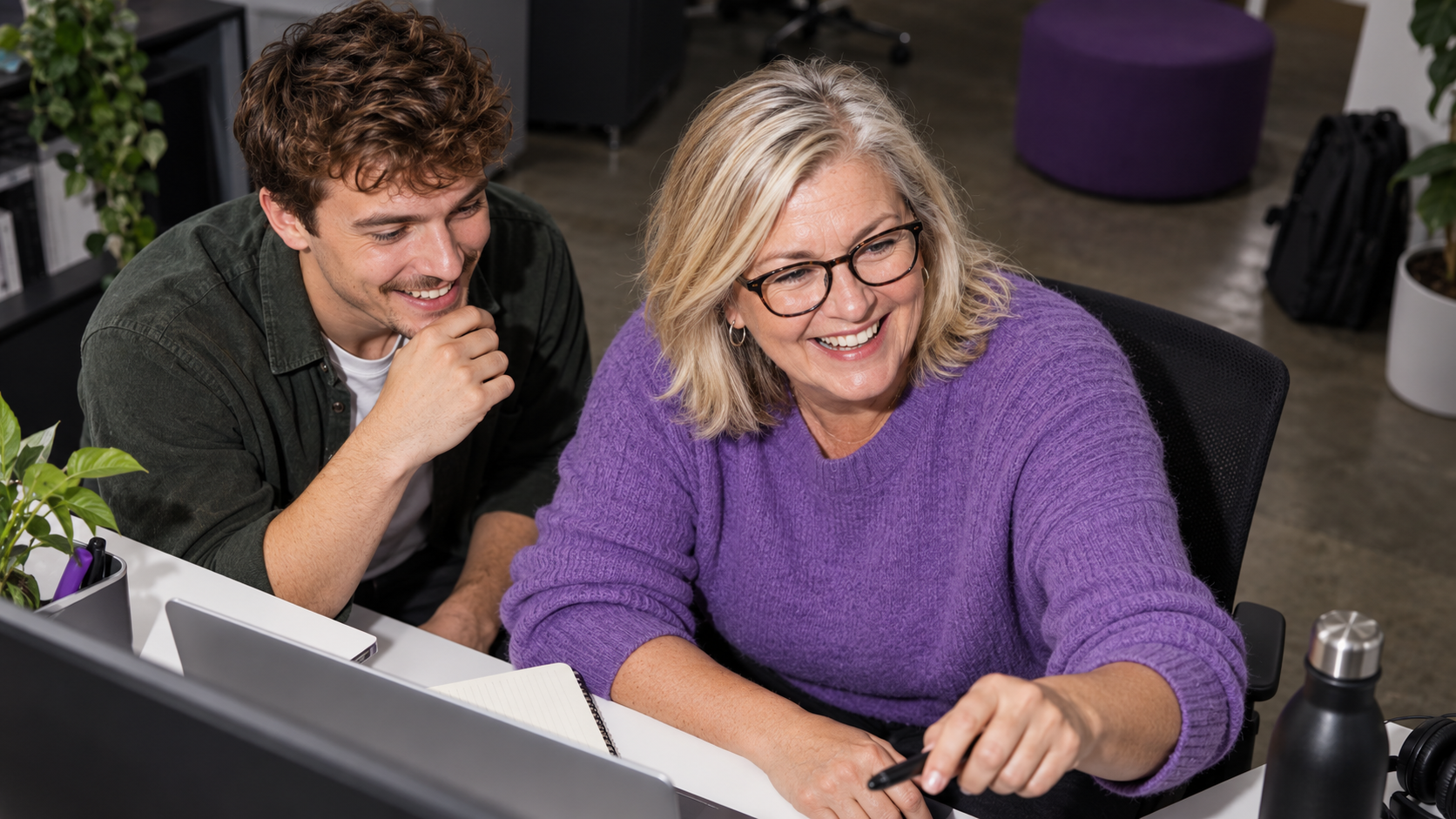 Ältere Frau und junger Kollege arbeiten gemeinsam am Computer an einem agentischen Workflow im Marketing.